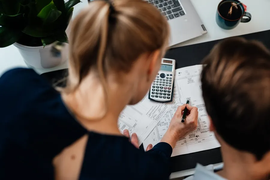 Zwei Personen planen am Schreibtisch mit Skizzen und Taschenrechner