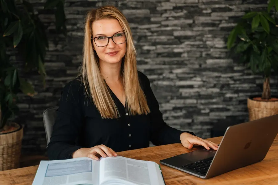 Frau mit Laptop und Unterlagen an einem Holztisch
