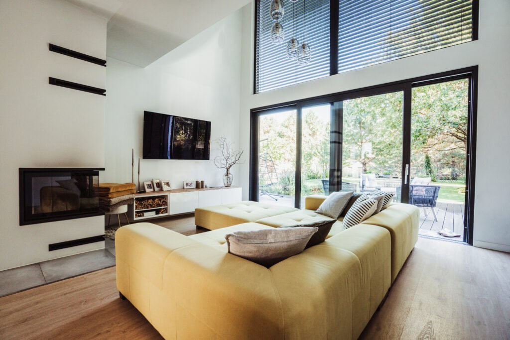 Wohnzimmer mit Kamin, gelbem Sofa und großer Fensterfront – Innenaufnahme Massivhaus Düngel