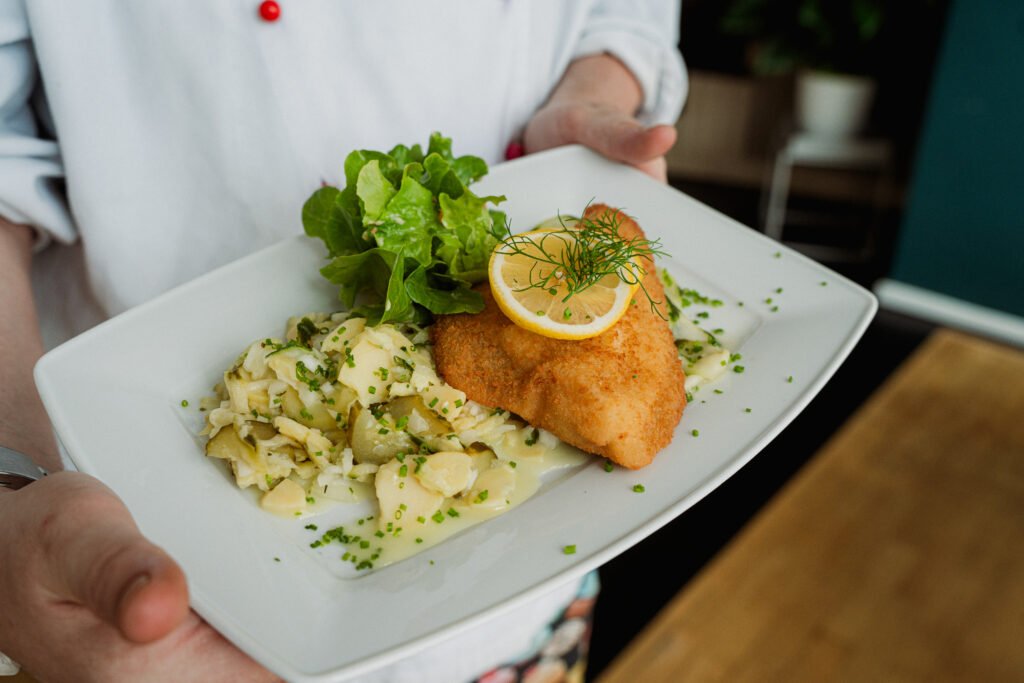 Koch präsentiert ein paniertes Filet mit Zitrone und Kartoffelsalat – Hotel Schwarzwald in Freudenstadt