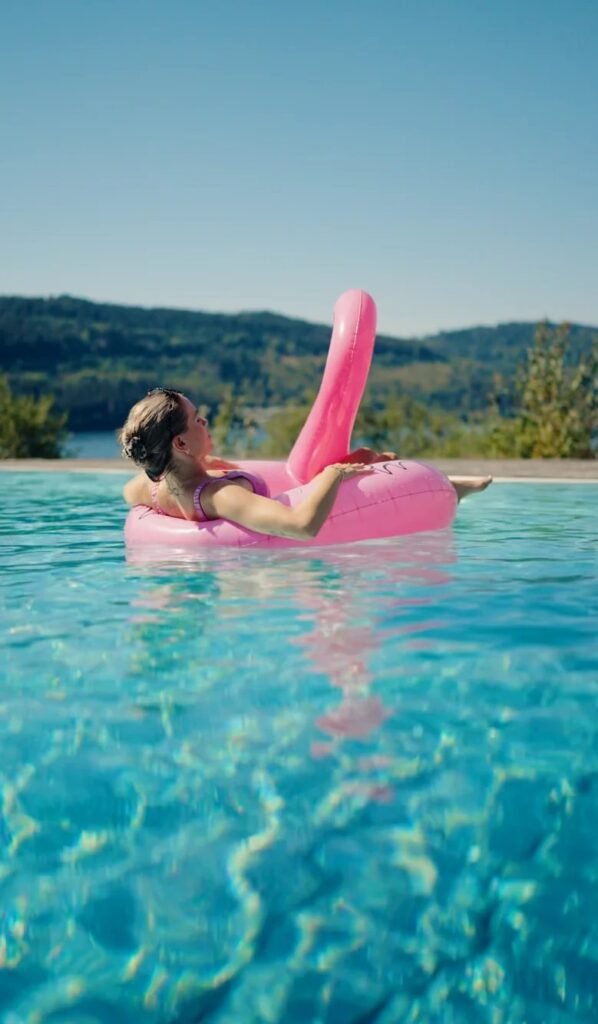 Frau auf einem pinken Flamingo im Pool mit Blick auf den See – Videostill aus dem Sommerdreh, Seehotel Wiesler